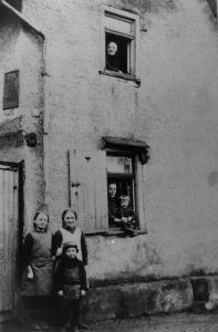 Gestern: Kirchstraße 16 um 1924, am Fenster oben Großmutter Charlotte Bohrmann, unten Familie Ludwig Fraund. Heute: Alt Langenhain 32, Vereinshaus des Heimat- und Gescbichtsvereins. Von der gegenüberliegenden Kirchturmsspitze aus gesehen